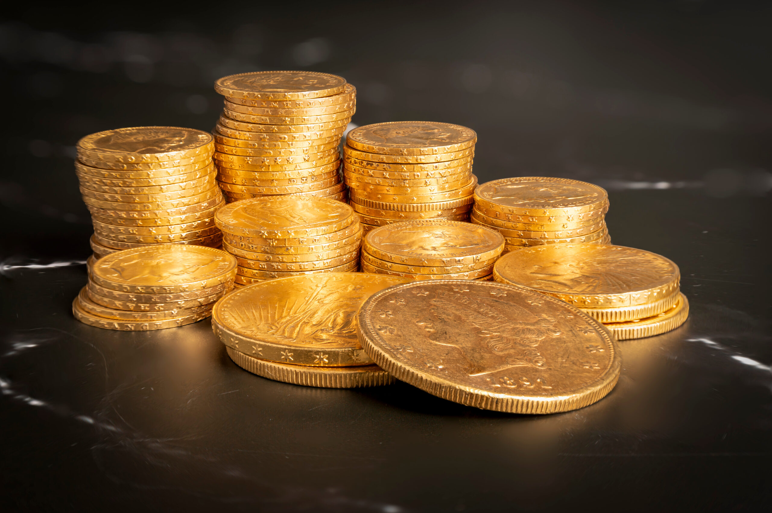 Paris, France – 03 26 2024: Still life. Close-up view stacks of golden Louis coins and american on a black and white marble surface.